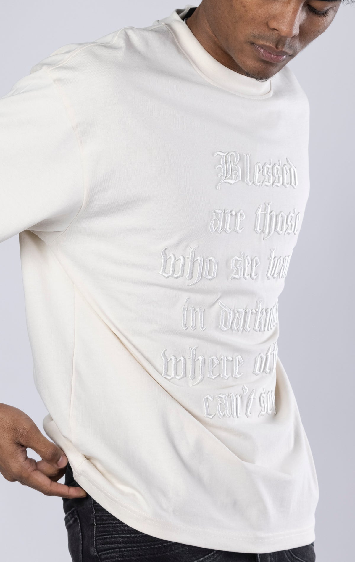 Blessed Darkness Boxy Tee. Cream t-shirt made from 100%  250gr cotton. Features a boxy fit, dropped shoulders, longer sleeves, a 3D embroidered front message, and subtle "blessed" branding